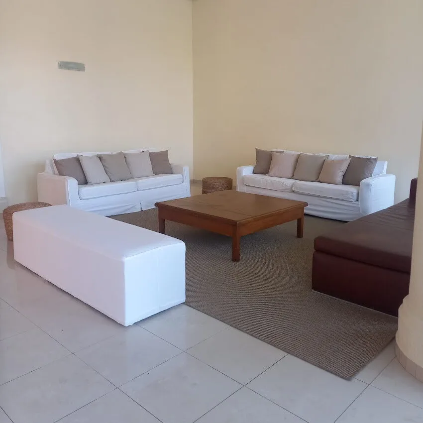 Lounge com sofás brancos, pufe longo branco e mesa de centro de madeira