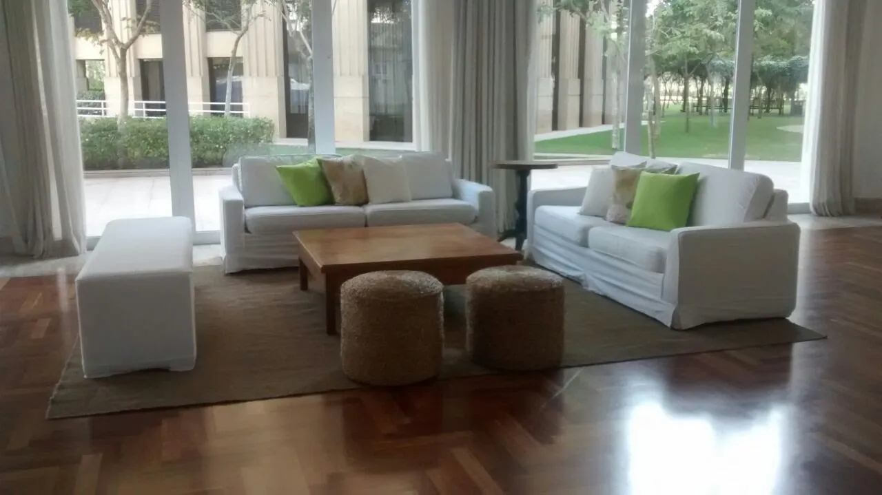 Lounge com sofás brancos, pufes de palha e almofadas verdes