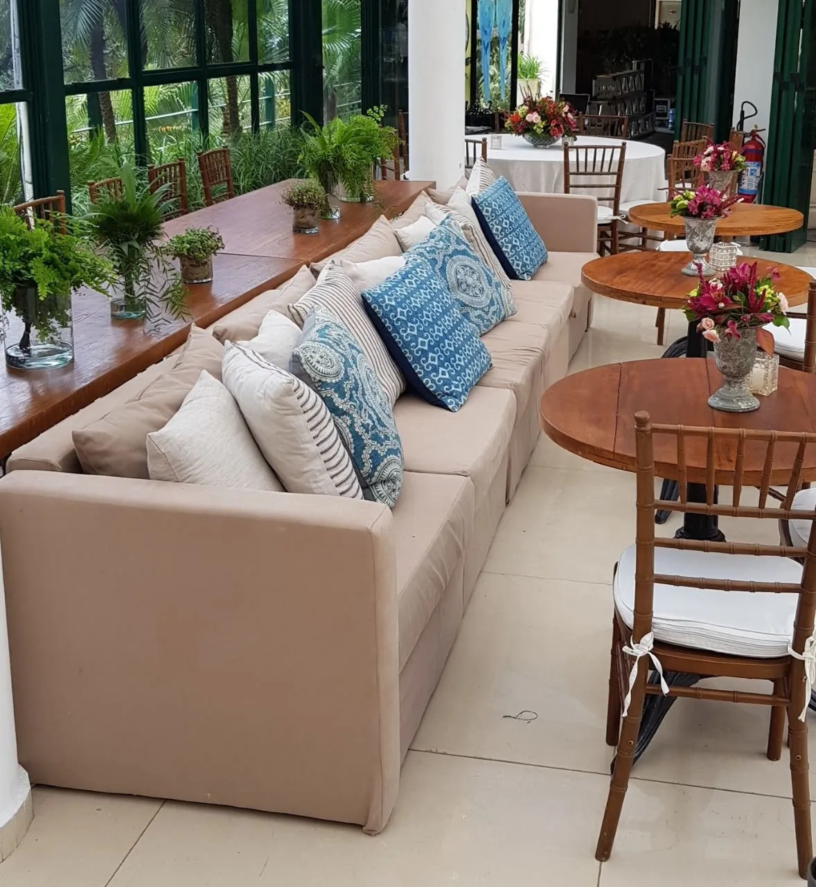 Sofá modular com almofadas azuis e bistrôs com cadeiras Tiffany