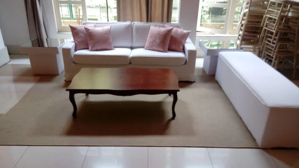 Lounge com sofá branco, pufe longo e almofadas rosé