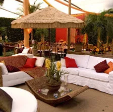 Lounge com ombrelone de palha, sofás brancos e almofadas vermelhas